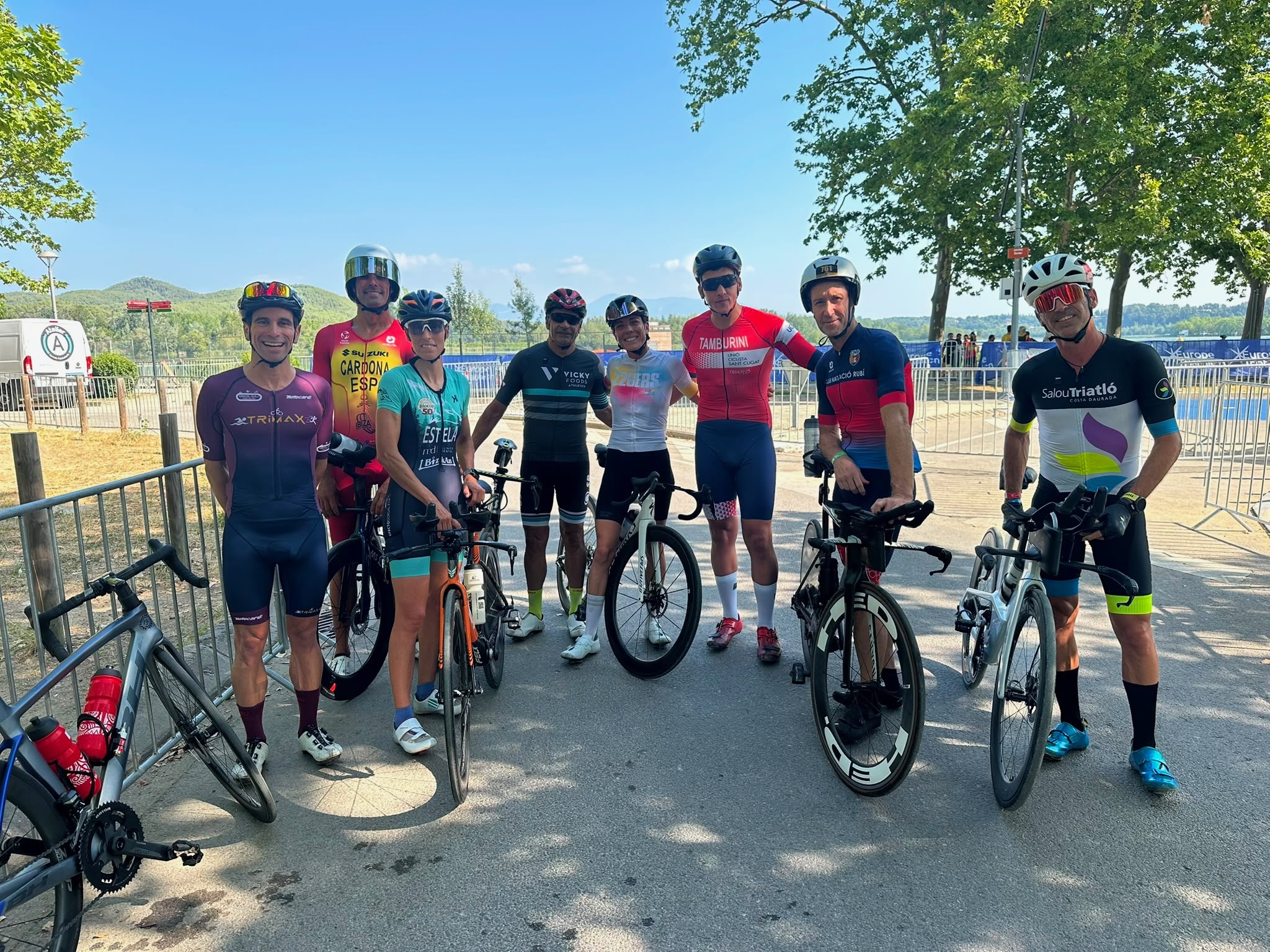 Group of cyclists posing with their bikes by Lake Banyoles after a ride