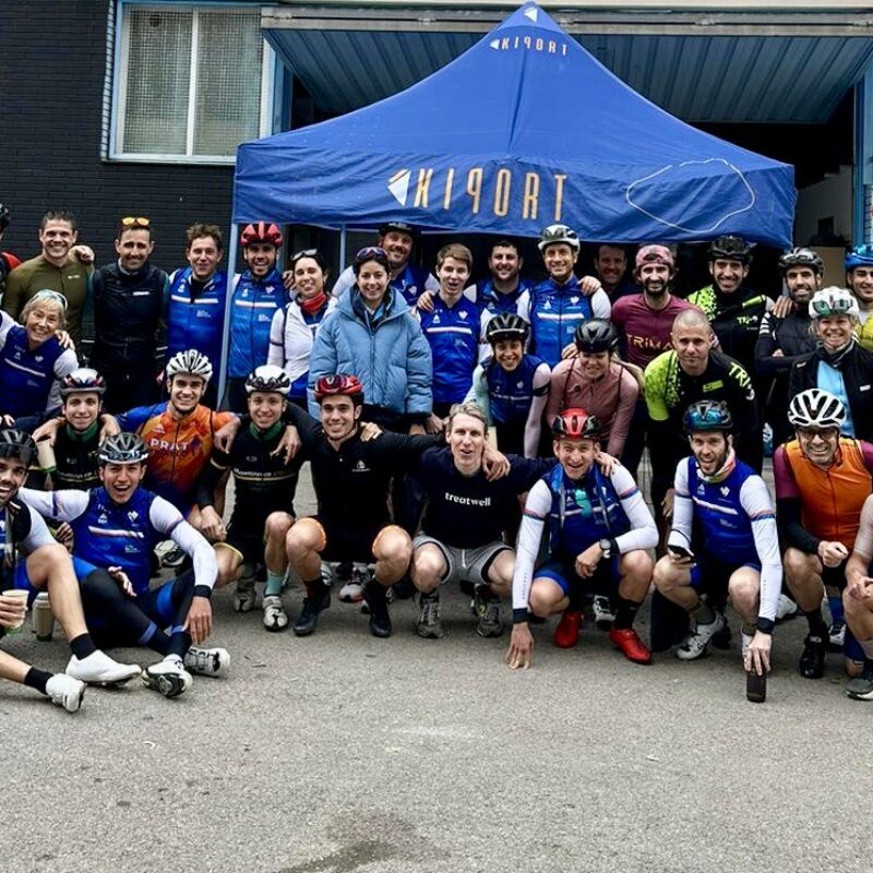 Gran grupo de ciclistas de club posando frente a una carpa tras un entrenamiento.