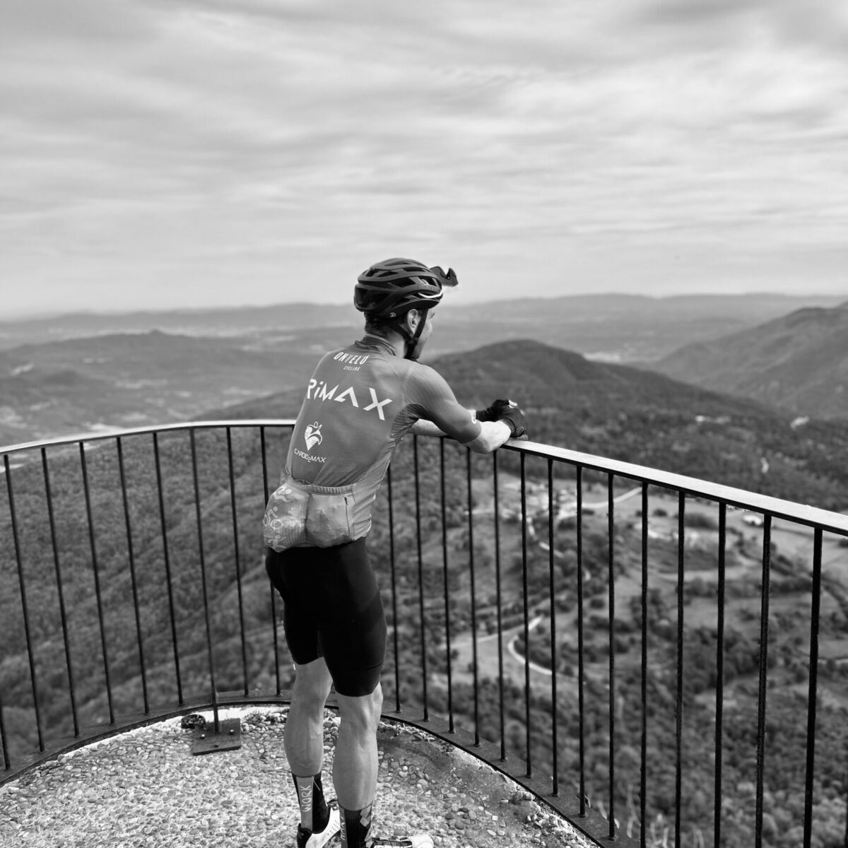 Cyclist in TRIMAX kit pausing at a mountain viewpoint during a ride