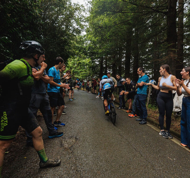 Ironman athlete riding through a wooded course lined with cheering spectators