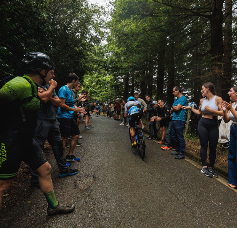 Ironman athlete riding through a wooded course lined with cheering spectators