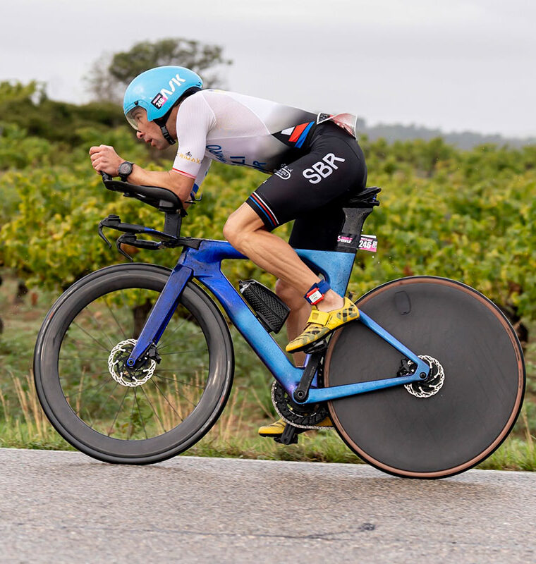 Triathlete riding a time trial bike through vineyards during a race